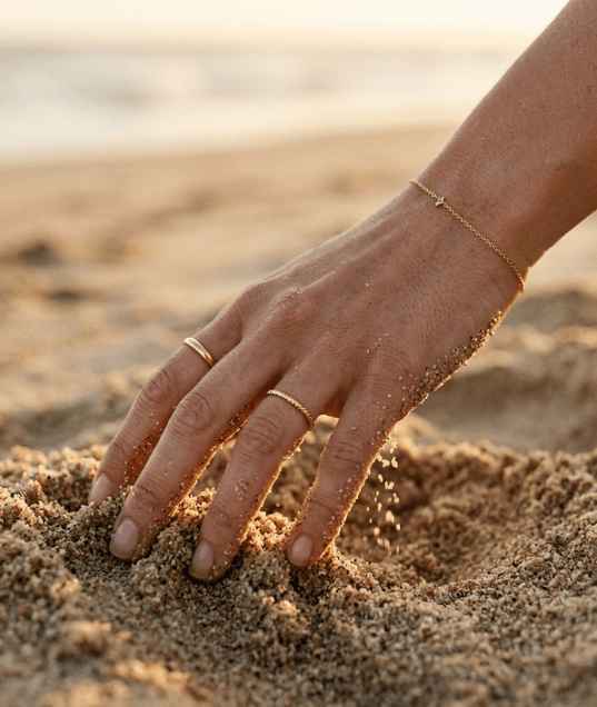A hand in the sand with jewelry